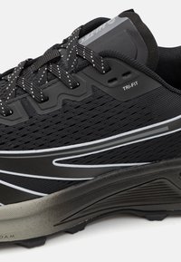 Zapatilla de running negra con parte superior de malla transpirable, acentos reflectantes y suela acolchada con una superficie texturizada. Detalle de diseño Tri-fit incluido.