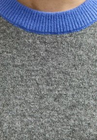 Grijze gebreide trui met een blauwe ribbelkraag. De stof is zacht en egaal van textuur en bestaat uit een mix van lichtgrijze en donkergrijze garens.