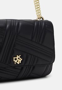 Czarna pikowana skórzana torebka na ramię z złotym łańcuszkiem. Zdobiona geometrycznym wzorem i złotym logo na przodzie.