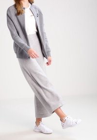 Cardigan grigio chiaro con scollo rotondo e bottoni frontali, abbinato a una lunga gonna grigia coordinata e scarpe da ginnastica bianche con dettagli ritagliati.