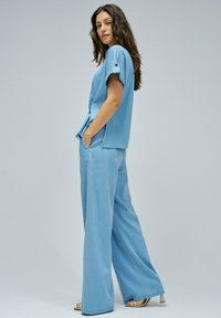 Completo in denim azzurro chiaro composto da una blusa corta a maniche corte e pantaloni a gamba larga. Il tessuto è morbido, con una superficie liscia e dettagli minimi.