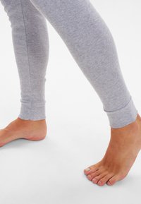 Gray cotton leggings with a slim fit, featuring fitted cuffs and soft texture. Bare foot visible, floor surface is plain.