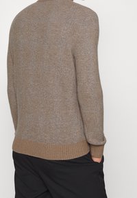 Brauner Strickpullover mit geripptem Saum und Bündchen. Weicher Stoff, Rundhalsausschnitt und dezentes Muster in einem gedämpften Farbton. Lockerer Schnitt.