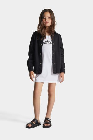 Svart knäppt jacka över en vit t-shirt med grafiskt tryck. Modellen har på sig en kort klänning och svarta slidesandaler.