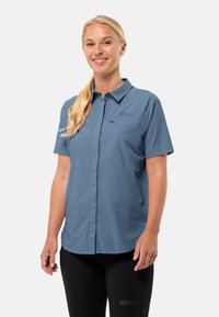 Short-sleeve, button-up shirt in light blue, made of a textured, breathable fabric. Features a single chest pocket and a logo on the left side.
