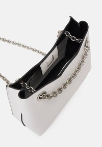 Bílá kabelka z veganské kůže s řetízkovým popruhem, která má černý interiér a elegantní, strukturovaný design. Otevřený vršek a minimalistické kovové detaily.