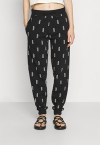 Zwarte joggingbroek met witte "HUGO" logo print, elastische tailleband en omgeslagen broekspijpen, gecombineerd met zwarte sandaaltjes met bandjes.