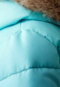 Chaqueta de plumas de color azul claro con un diseño acolchado horizontal y un cuello de piel sintética marrón. Textura suave con detalles de costura visibles.