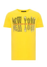 Gelbes T-Shirt aus Baumwolle mit einem grafischen Druck, auf dem "NEW YORK" in Schwarz und Rot steht. Kurze Ärmel und runder Halsausschnitt.