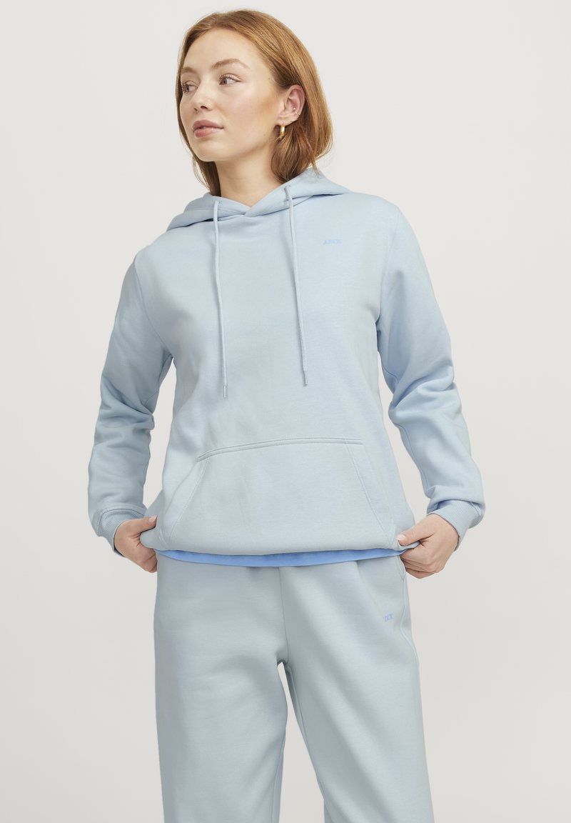 Felpa leggera blu con tasca frontale, cappuccio con cordino e polsini a coste. Abbinata a pantaloni della tuta leggeri blu coordinati. Tessuto morbido e casual.