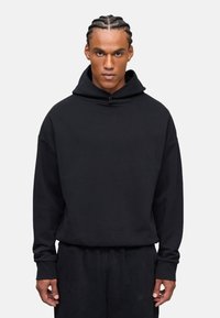 Sudadera negra con capucha en un corte holgado. Confeccionada en una tela suave, con mangas largas y puños acanalados. Presenta un sutil detalle de logo en el dobladillo.