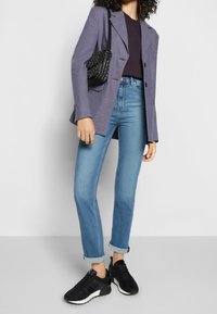 Blazer de cuadros en púrpura y azul, combinado con una blusa azul marino, jeans de un azul claro y zapatillas negras. Los acabados incluyen puños remangados y un bolso.