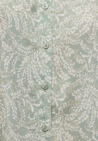 Mint green shirt with a floral pattern in white, featuring five light-colored buttons down the front and a smooth, lightweight fabric texture.