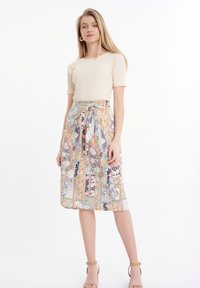 Top corto a maniche corte color beige a coste abbinato a una gonna a fantasia multicolore con vita regolabile, silhouette fluida e accenti floreali.