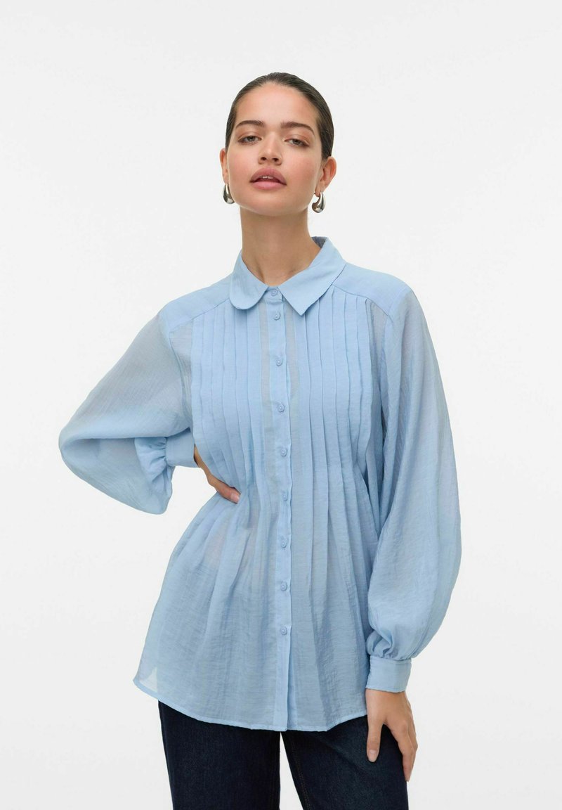  Lichtblauwe blouse met lange mouwen, kraag en verticale strepen, met knoopsluiting aan de voorkant. Heeft pofmouwen en een ontspannen pasvorm.