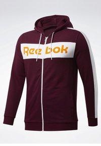 Felpa con cerniera color bordeaux, con una striscia bianca e il logo 'Reebok' in arancione. Presenta un cappuccio, cordini e tasche frontali. Tessuto morbido.