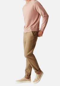 Světle růžová mikina s kulatým výstřihem, raglánovými rukávy a postranním rozparkem. Béžové tapered kalhoty s kapsami. Béžové šněrovací tenisky.