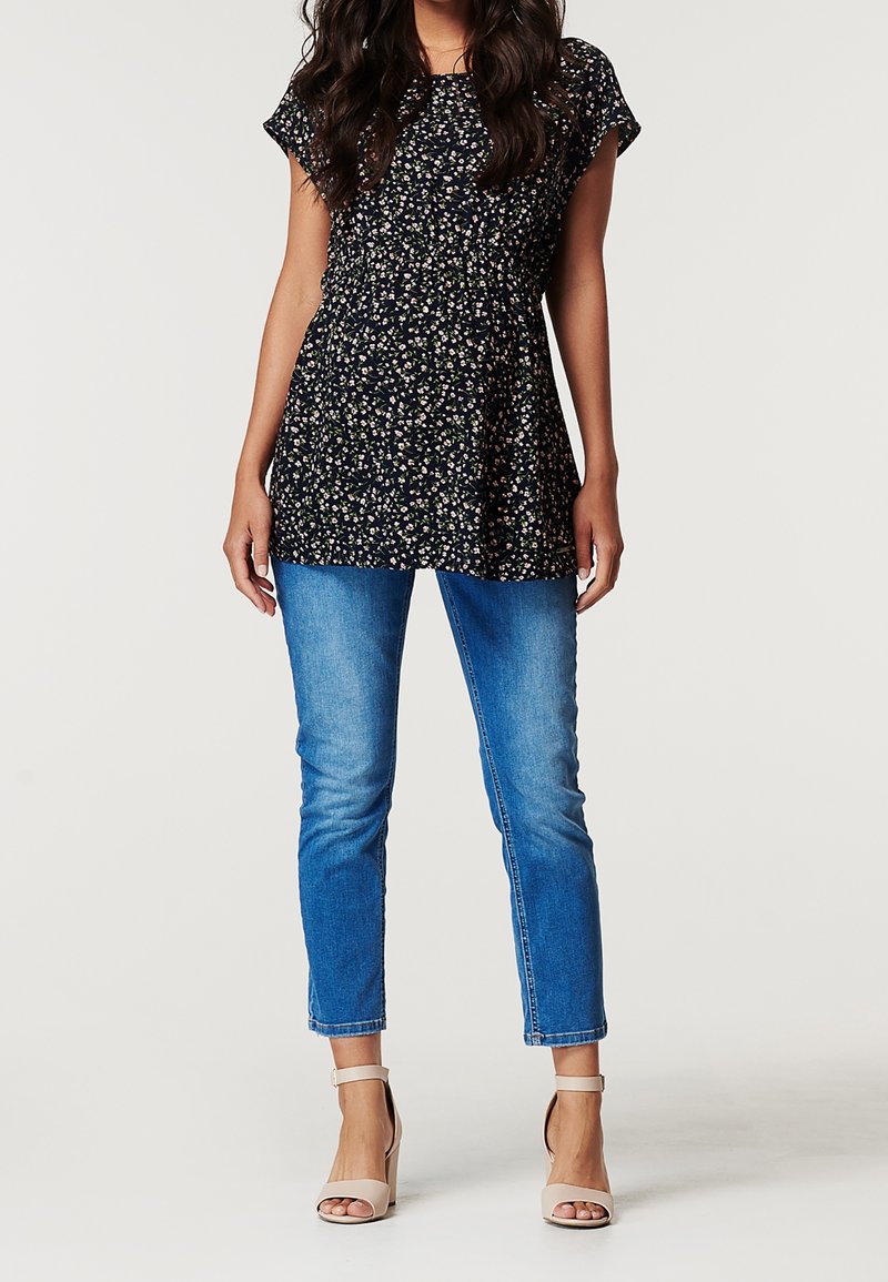 Marinblå blommönstrad tunika med korta ärmar, samlad midja, i kombination med ljusblå skinny jeans och nakna ankelremmar.