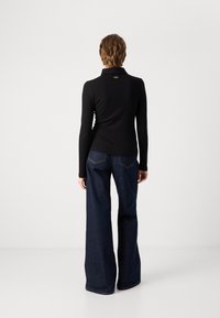 Zwart langemouwen top met een kraag en een gouden label, gecombineerd met flared donkerdenim jeans met zichtbare stiksels en een relaxed fit.