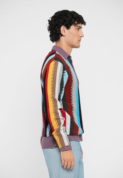 Colorful knit sweater with vertical stripes in red, blue, gray, and brown. Features a crew neck and long sleeves; worn over a purple collared shirt.