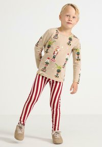 Beige langærmet skjorte med nøddeknækker-tryk, parret med rød og hvid stribet leggings. Outfittet har en behagelig pasform og et afslappet design.