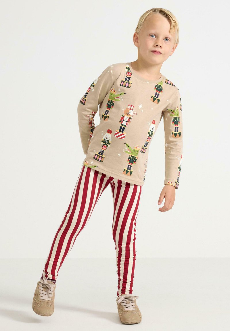 Beige langærmet skjorte med nøddeknækker-tryk, parret med rød og hvid stribet leggings. Outfittet har en behagelig pasform og et afslappet design.