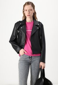Svart faux skinn bikerjakke med sølvglidelåser og trykknapper, båret over en rosa grafisk T-skjorte og grå jeans. Enkel, minimalistisk design.