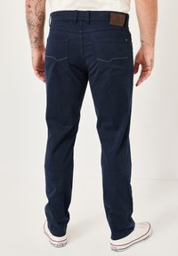 Navy blue cotton trousers feature a straight cut, back pockets with a curved design, and a brown leather patch at the waistband.