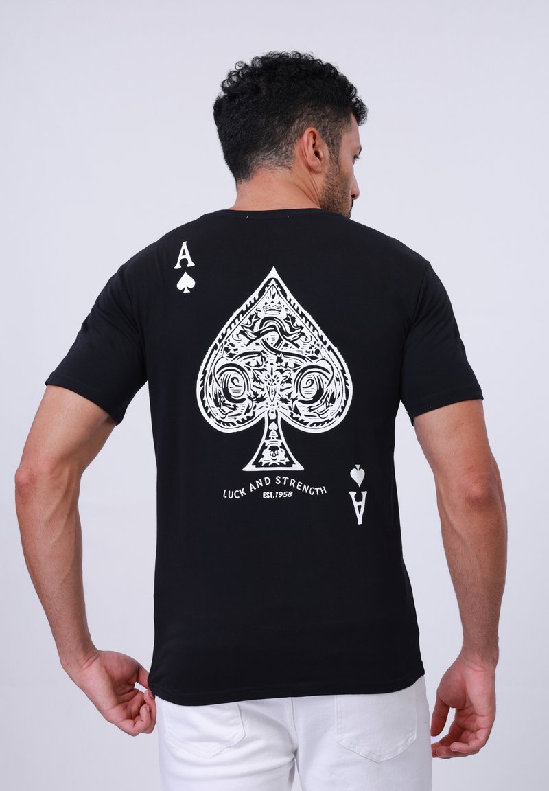 T-shirt noir avec un grand motif de pique blanc au dos, orné de volutes et du texte "Chance et Force ÉTABLI. 1958."
