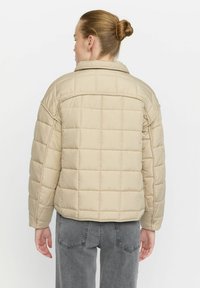 Beige polstret jakke med quiltet design, bred krave og kort længde, der har lange ærmer og en glat, let tekstur.