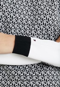 Maglione bianco con polsini a coste neri, caratterizzato da un motivo geometrico in bianco e nero su tutto il corpo. Dettaglio logo piccolo sul polsino.