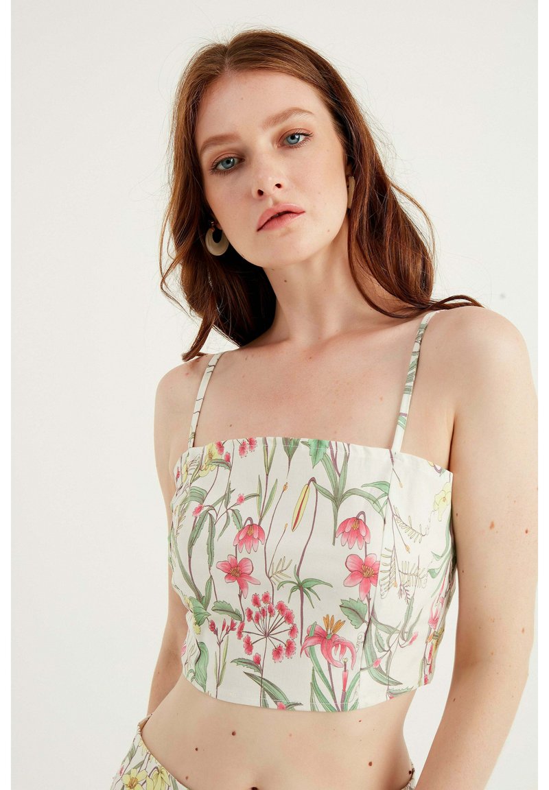 Crop top med tunna band, med ett blommönster i rosa och grönt på en vit bakgrund. Slätt tyg; fyrkantig halsringning.