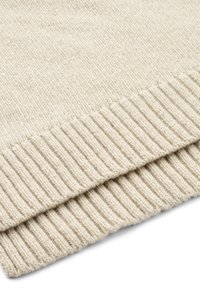 Primer plano del dobladillo de un suéter beige de punto que muestra la textura acanalada y el detalle de la tela suave de lana.