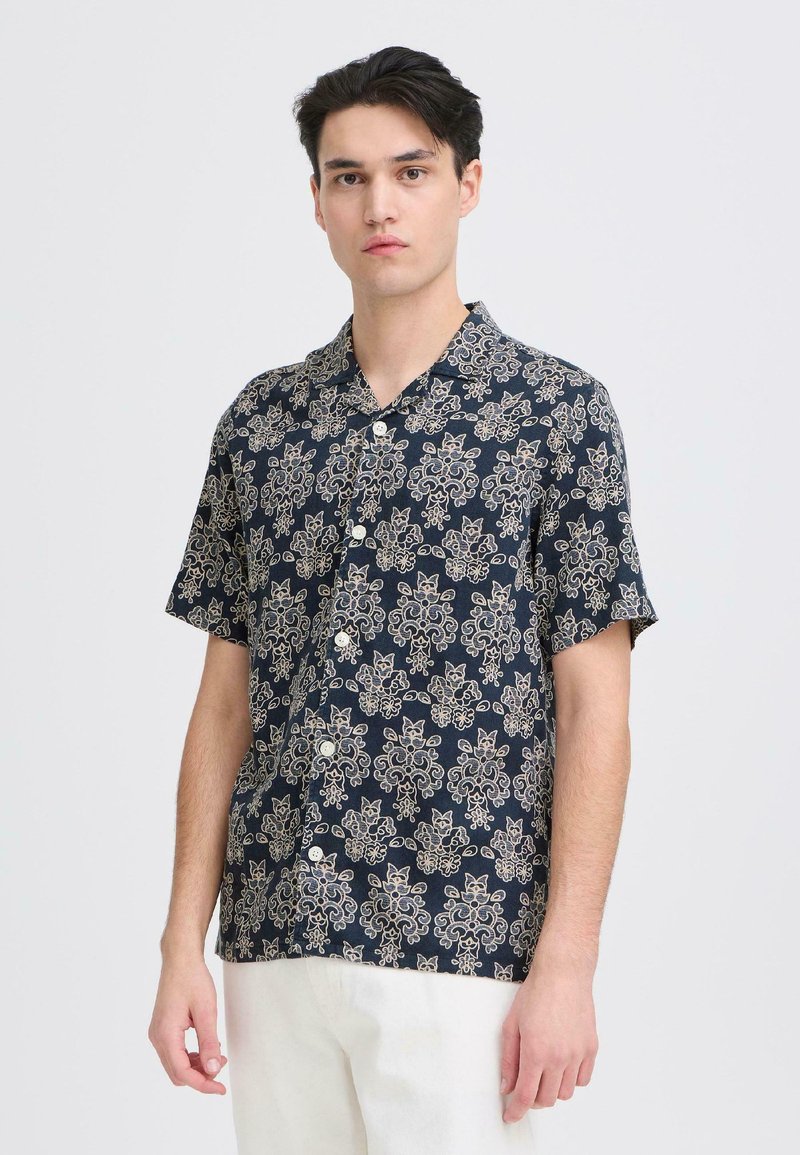 Πουκάμισο με κοντά μανίκια σε ναυτικό μπλε χρώμα, με κρέμ μοτίβο λουλουδιών και γατών. Η υφή του υφάσματος φαίνεται ελαφριά και αεριζόμενη.