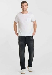 T-shirt blanc en coton avec une poche, associé à un jean en denim foncé. La tenue est complétée par des baskets blanches avec des accents marron.