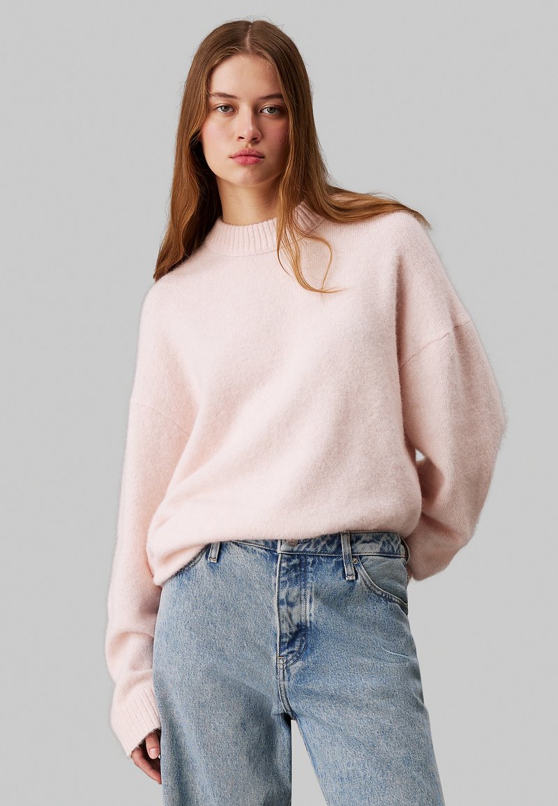 Maglione oversized rosa chiaro in lana con collo a girocollo a coste e spalle cadenti, abbinato a jeans in denim azzurro chiaro a vita alta.