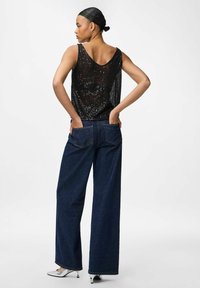 Top in paillettes nere con schiena bassa, abbinato a jeans in denim blu scuro larghi. Tacchi a punta argentati completano il look.