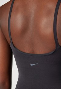 Crni sportski top s tank trakama, sa suptilnim Nike logotipom u sivoj boji na području grudi. Glatka, rastezljiva tekstura tkanine.
