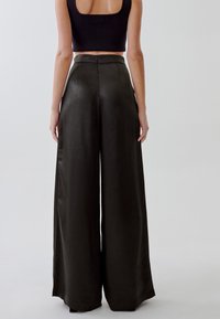 Pantaloni a vita alta, a gamba larga in satin verde scuro con una texture morbida e un leggero lucido; presentano una chiusura con zip sul retro.