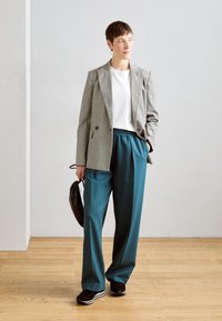 Grå hundtandmönstrad kavaj över en vit t-shirt, parat med tealbyxor. Tillbehören inkluderar en svart väska och mörka sneakers. Bakgrunden är av trä.