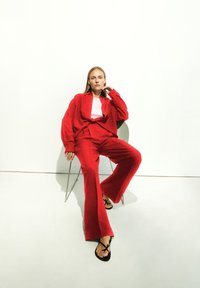 Rode linnen shirt en wijde broek met een gladde textuur. Draag een roze aansluitend top en zwarte sandalen met bandjes, zittend op een stoel.