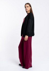 Czarna, oversize kurtka z długimi rękawami, połączona z szerokimi, burgundowymi spodniami. Gładka faktura, prosty design i brak widocznych wzorów.