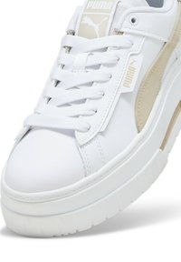 Zapatilla blanca de cuero con acentos de ante beige, suela de goma y punta redonda. Cuenta con cordones blancos planos y un logo en la lengüeta.