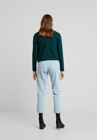 Tyrkysová zkrácená bunda s texturovaným vzorem, v kombinaci s světle modrými džíny. Černé kotníkové boty na blokovém podpatku dotvářejí outfit.