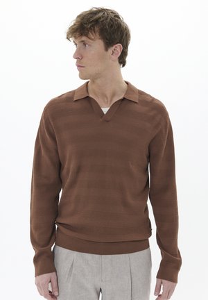 Suéter marrón de manga larga y cuello, con un patrón de rayas texturadas y un diseño de escote en V profundo, que complementa unos pantalones claros.