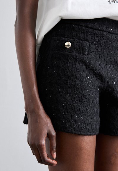 Shorts noirs texturés avec un motif subtil et des paillettes, dotés d'une poche avant et d'un accent en bouton doré. Le tissu semble doux et structuré.