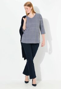 Oberteil mit Marine- und Weißkaro-Druck und Dreiviertelärmeln, kombiniert mit dunklen Jeans und marineblauen Pumps, und darüber eine schwarze Jacke.