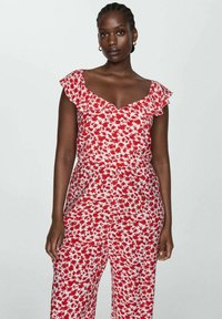 Červený a bílý květinový overal s volánovými rukávy, s V-výstřihem a volným střihem, vyrobený z lehkého materiálu s jemnou texturou.