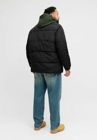 Musta toppatakki, jossa vihreä huppu, tikattu malli, rento istuvuus ja joustavat hihansuut, yhdistetty vaaleansinisiin farkkuihin ja puukenkätyyppisiin sandaaleihin.