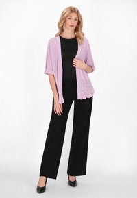 Cardigan in un morbido color lavanda con apertura frontale, maniche corte e motivo a rombi testurizzato, abbinato a una maglietta nera e pantaloni neri a gamba larga.